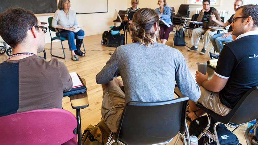 A group of people is gathered inside a classroom. They are sitting on chairs in a circle.