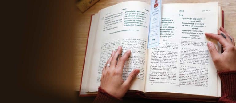 Person’s hands resting on an open book of Sanskrit or yoga text, symbolizing study and learning for Naropa University’s Graduate Yoga Studies low-residency program.