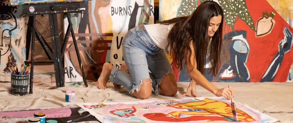 Paula Gasparini-Santos painting a work of art on a canvas resting on the floor