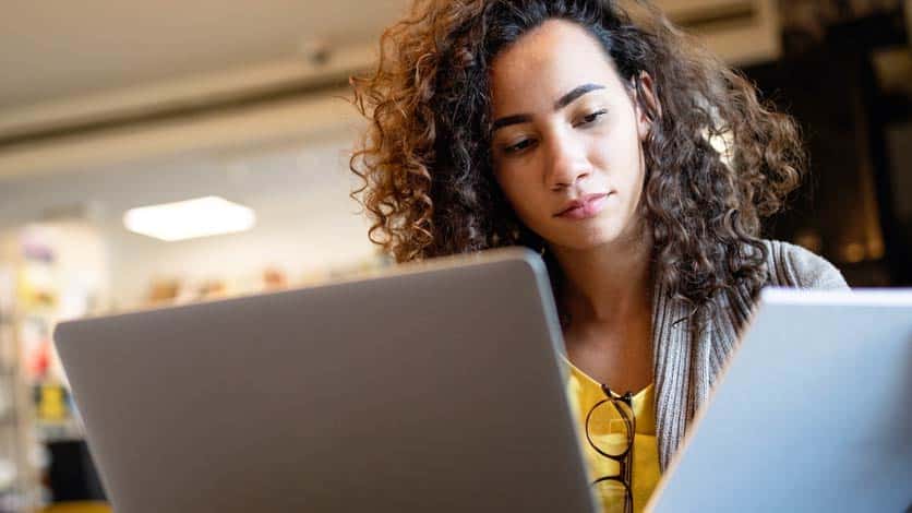 A young woman with curly hair looks intently at the screen of a tablet or laptop