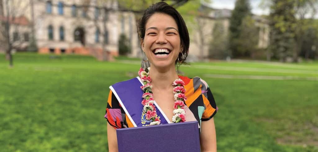 Woman with huge grin on her face holding a diploma from Naropa University.
