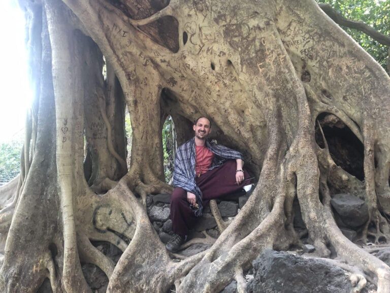 Daniel Rajunov sitting on the roots of an ancient tree