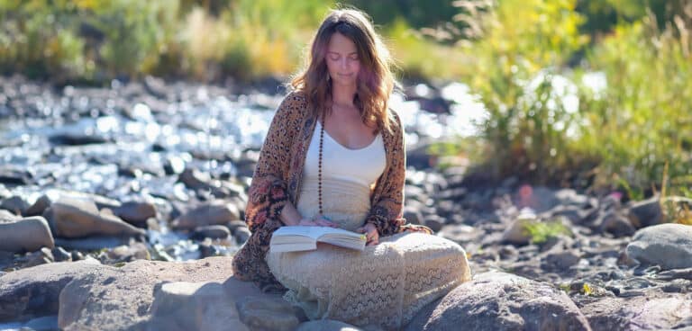 Kendall Higgins sitting by a river reading a book