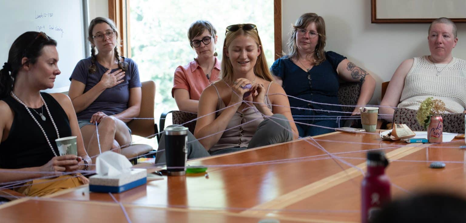 A group of people sitting around a table passing around a ball of yarn