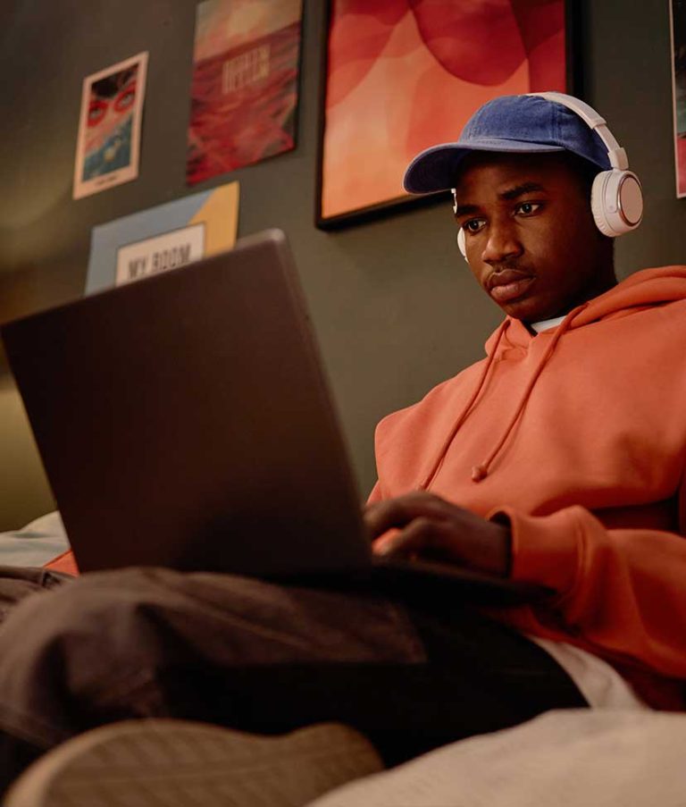 A man sitting on a couch using a laptop and wearing headphones