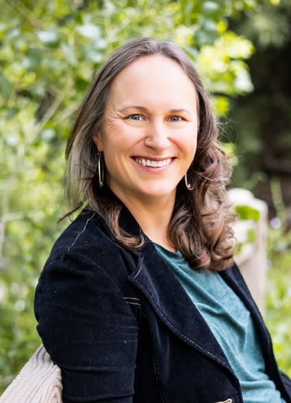 A woman leaning against a fence and smiling at camera