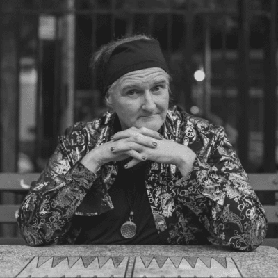 CAConrad with hands clasped sitting at a table