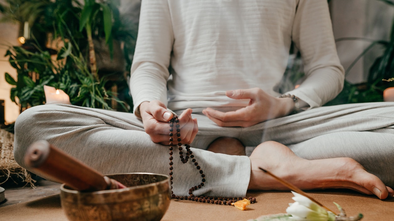 A person wearing white in lotus posture holding mala beads